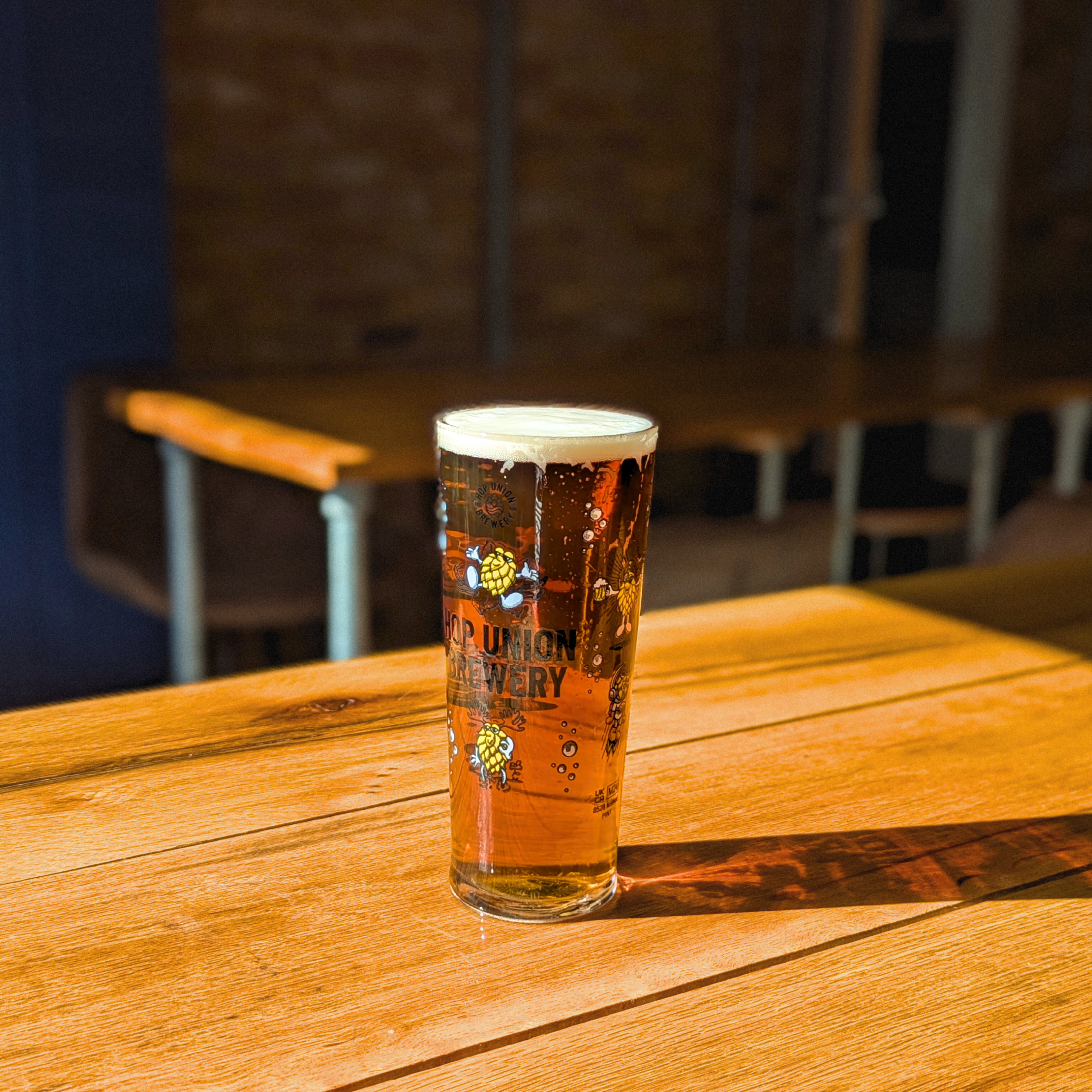 Exhibitionist American Red Ale beer in a Hop Union Brewery glass on a wooden table in the brewery's Bristol taproom bathed in sunlight