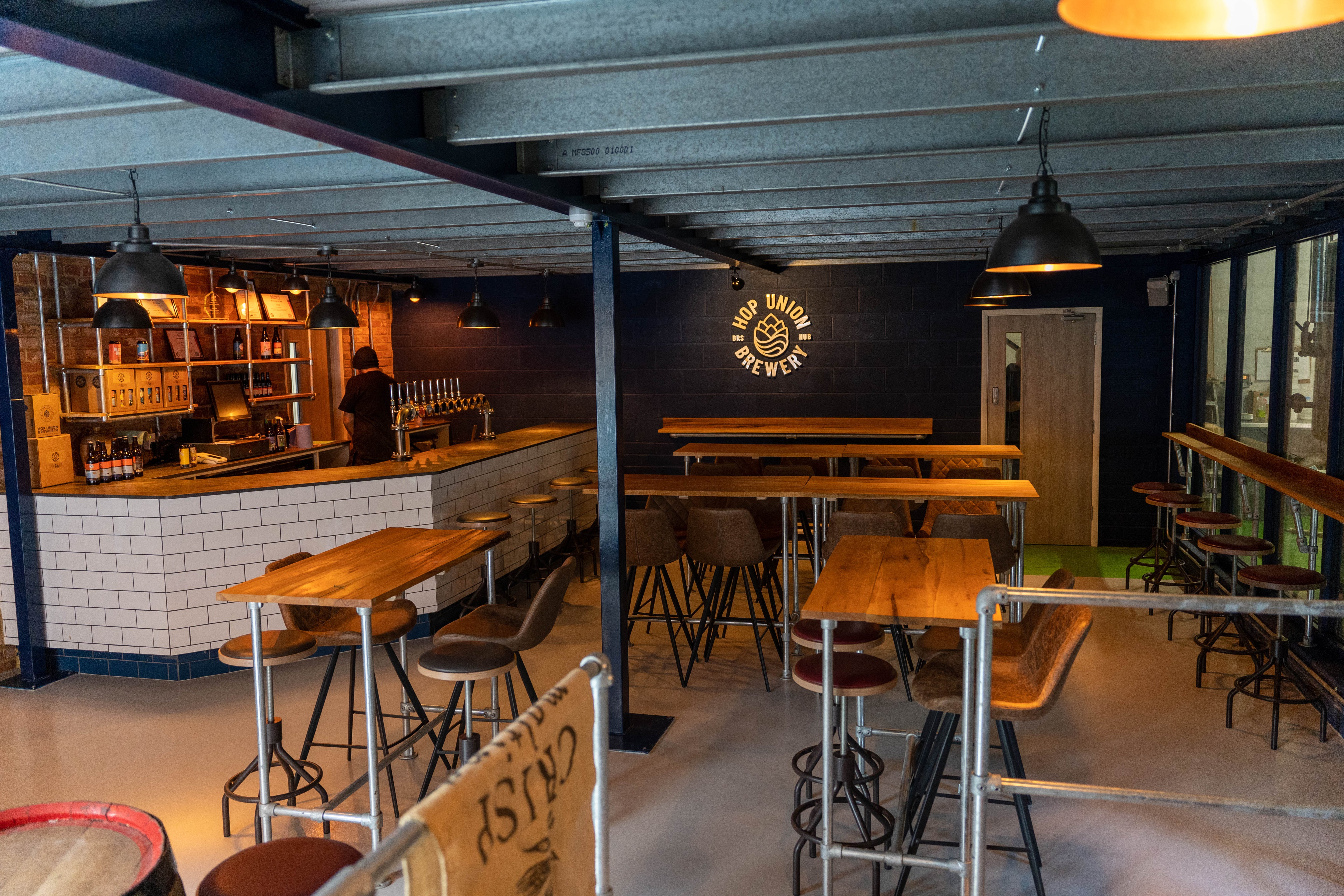 Interior of Hop Union Brewery Bristol taproom pub with wooden tables, stools, and a bar area.