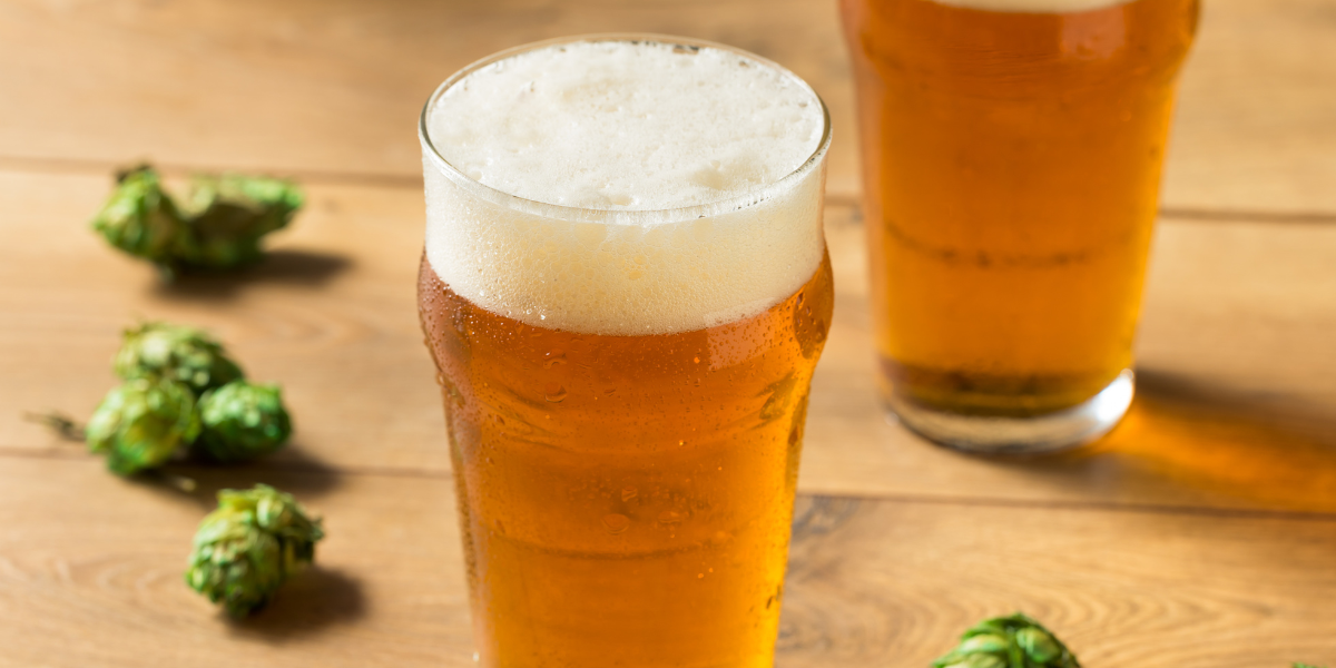 Two IPA beers on a table surrounded by hop flowers