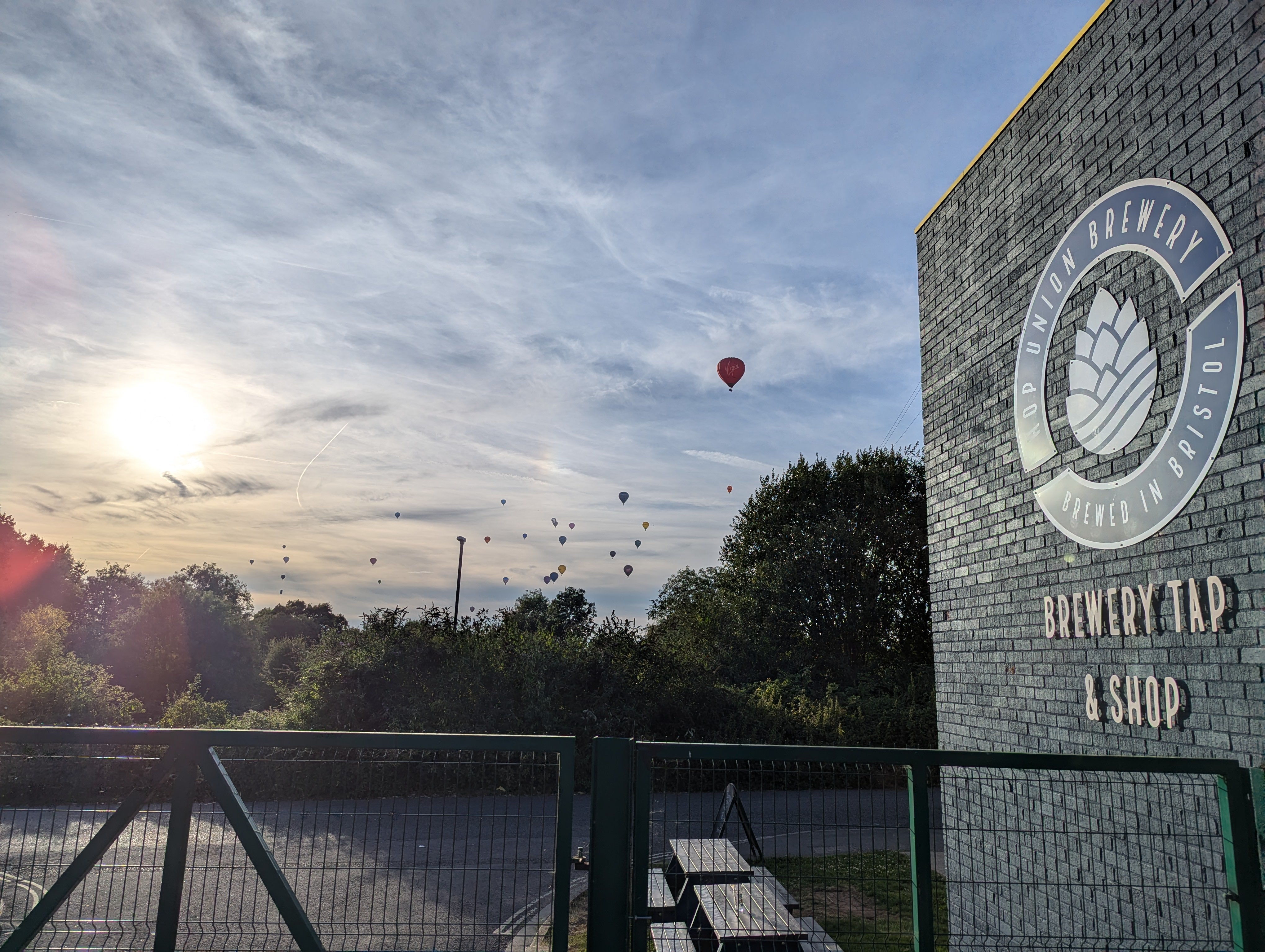 A photo of the sun highlighting the Hop Union Brewery logo on the outside taproom wall. In the background there is hot air baloons in the sky from the Bristol hot air balloon feista