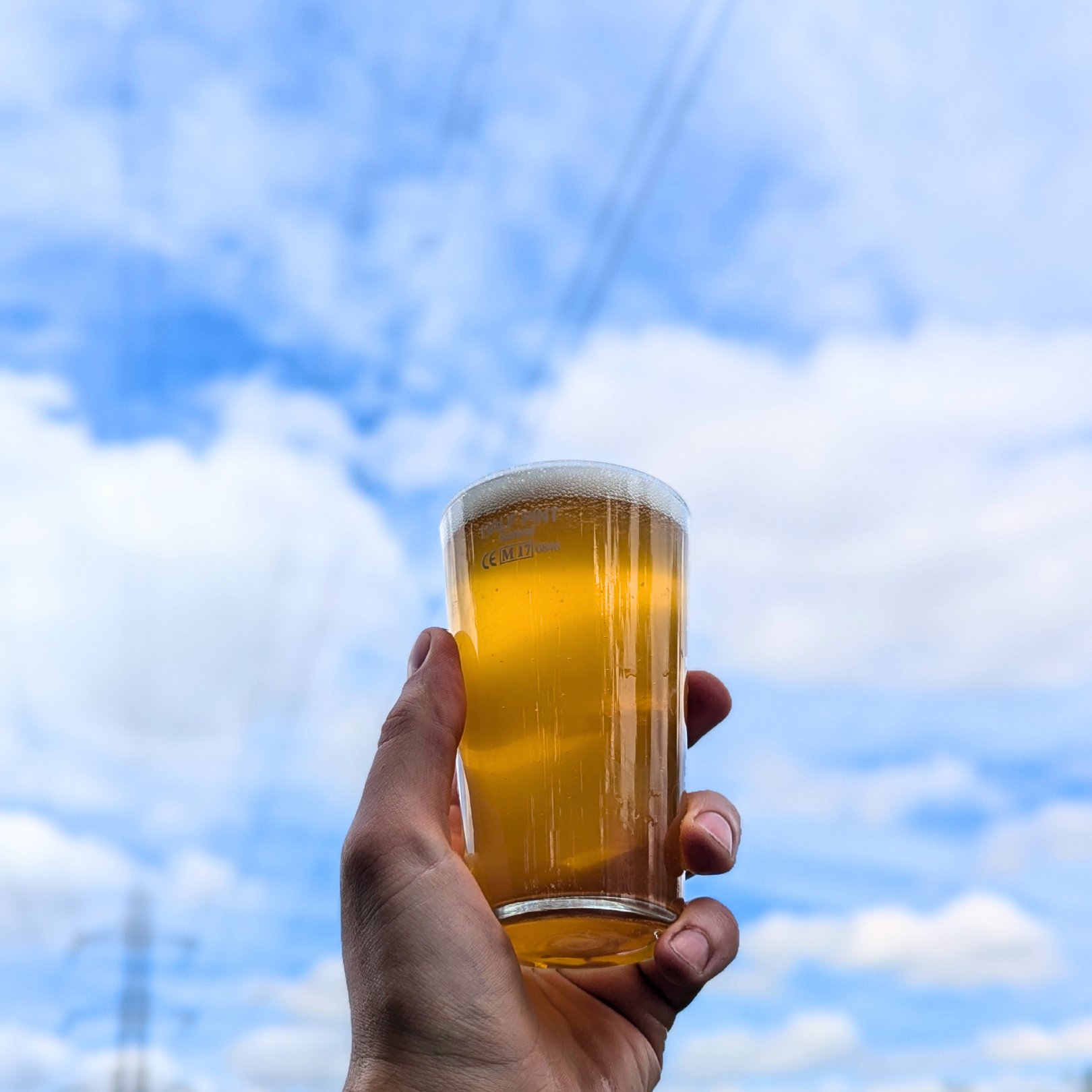 Hnd holidng a half pint of Hop Union Brewery beer in front of a blue sky