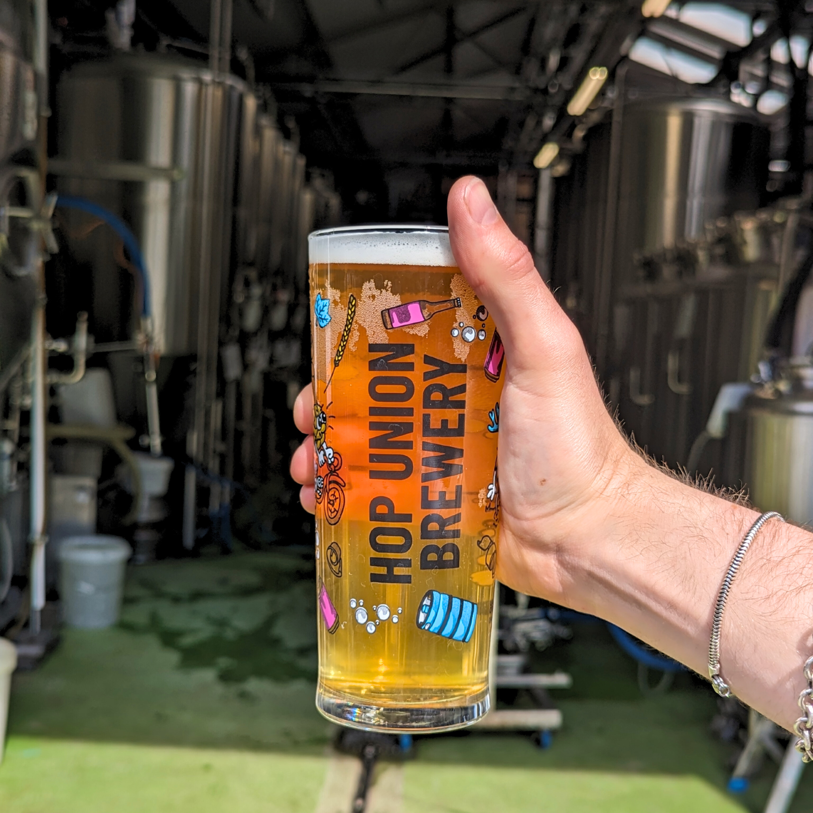 hand holding up a pint of beer in a Hop Union Brewery branded glass in front of their Bristol brewery