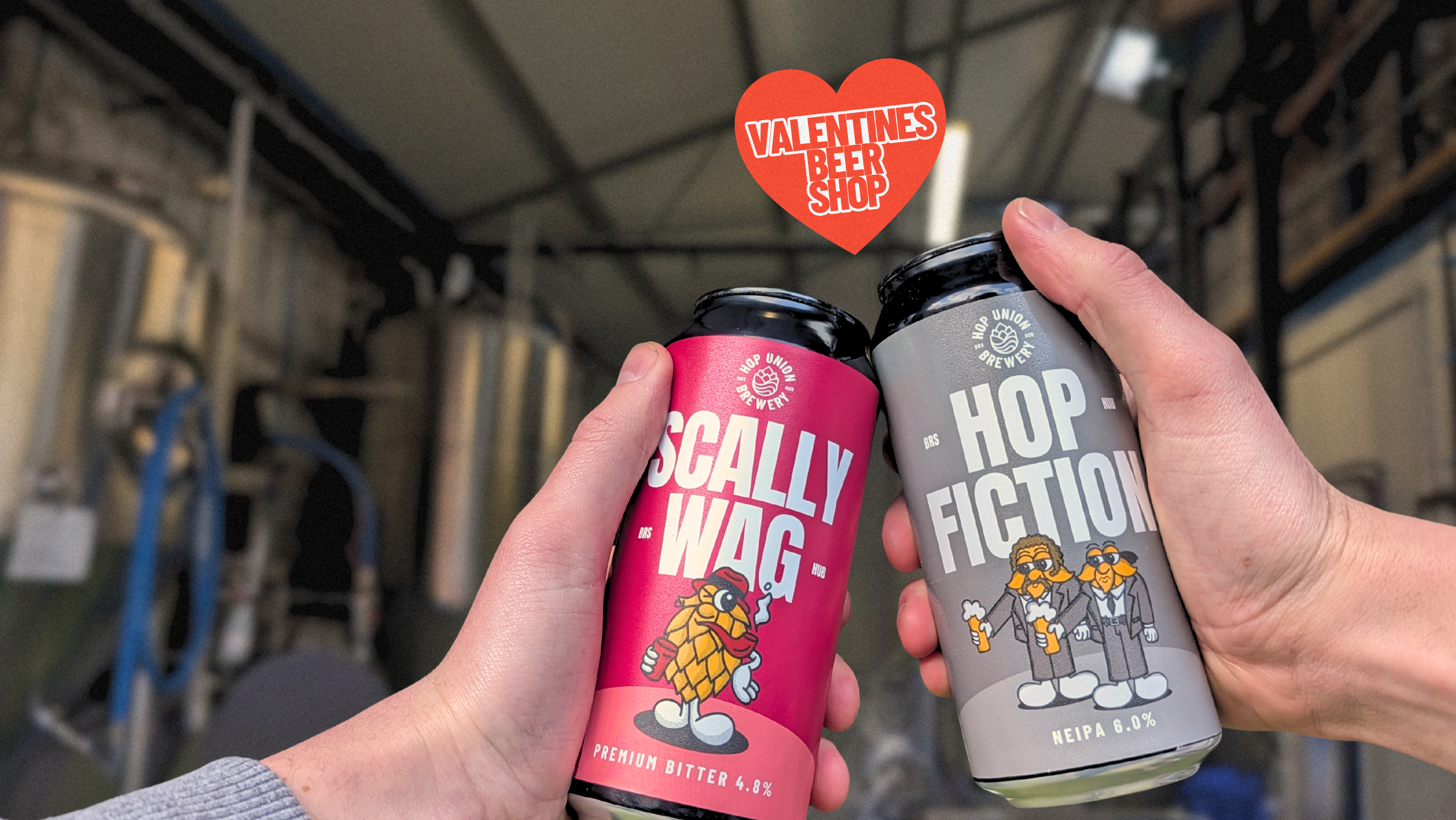 Two cans of Hopn Union Brewery beer, Scallywag and Hop Fiction, held in front of a brewery with a heart-shaped Valentine's Day sign.